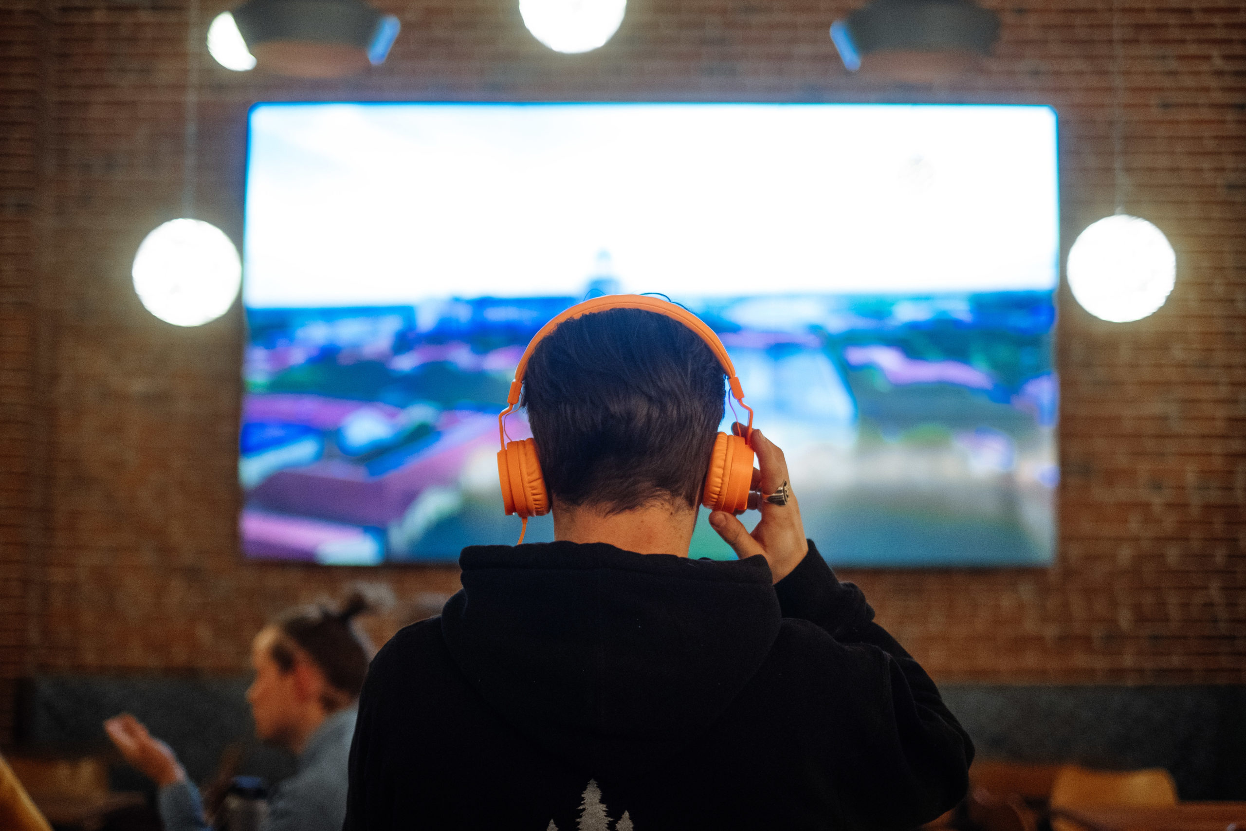 How to Provide Social Distance Entertainment Options As Restaurants Reopen - AudioFetch Audio Over WiFi Man with Headphones Watching TV in Sports Bar - Audio Over WiFi Streaming